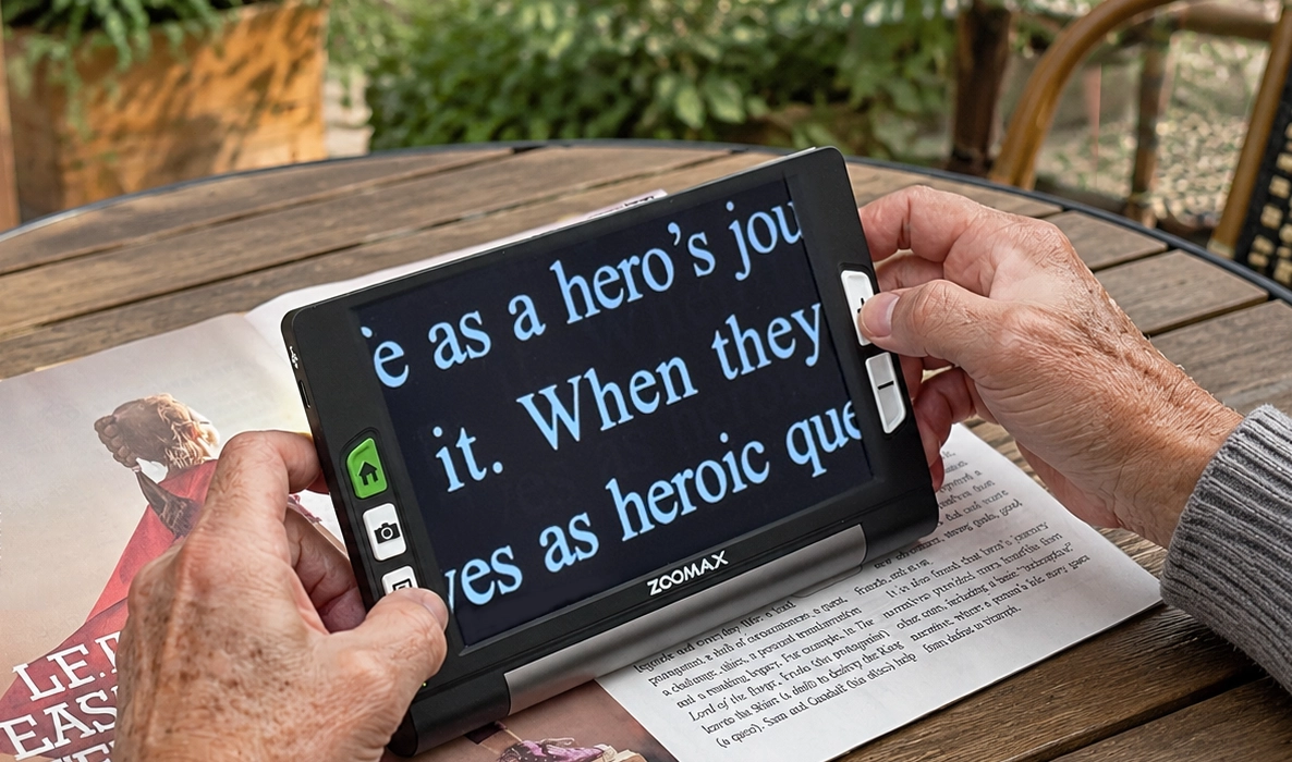 elderly cataracts and mild glaucoma patient using zoomax luna 8 handheld device digital magnifier for reading at an open air cafe