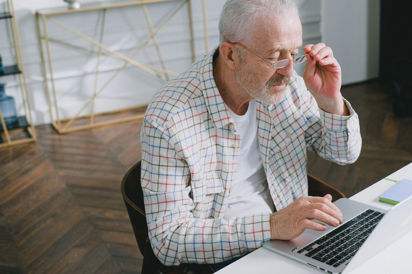 senior man adjusting his eyeglasses while checking information on a laptop at a desk in a home interior